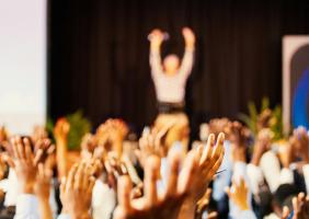 Hands raised to the sky with an out of focus human with arms raised in the background
