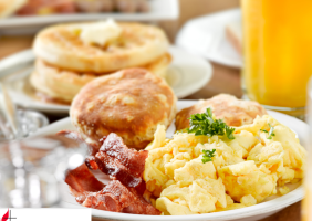 Picture of a breakfast plate with bacon, scrambled eggs, and a biscuit with a glass of orange juice