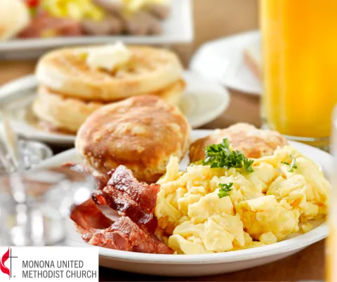 Picture of a breakfast plate with bacon, scrambled eggs, and a biscuit with a glass of orange juice
